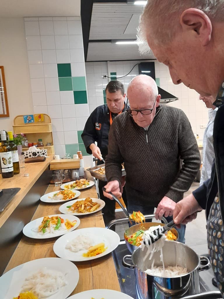 Oosterse avond: noedels uit de pan scheppen en borden vullen met oosterse gerechten.